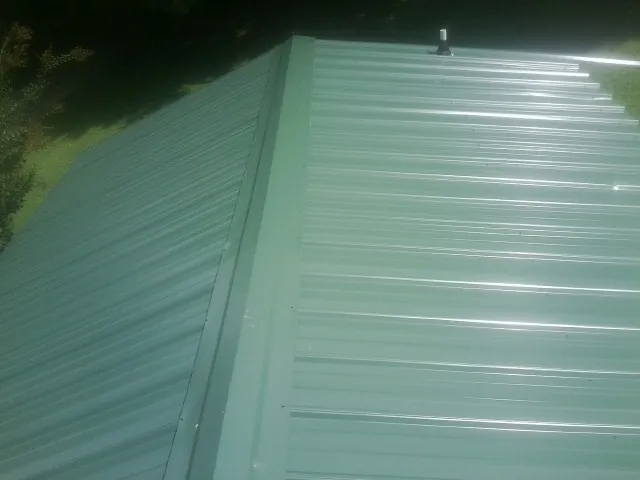New green metal panels meeting at the ridge of a roof — Flat Roof Repair work by our crew in Weston